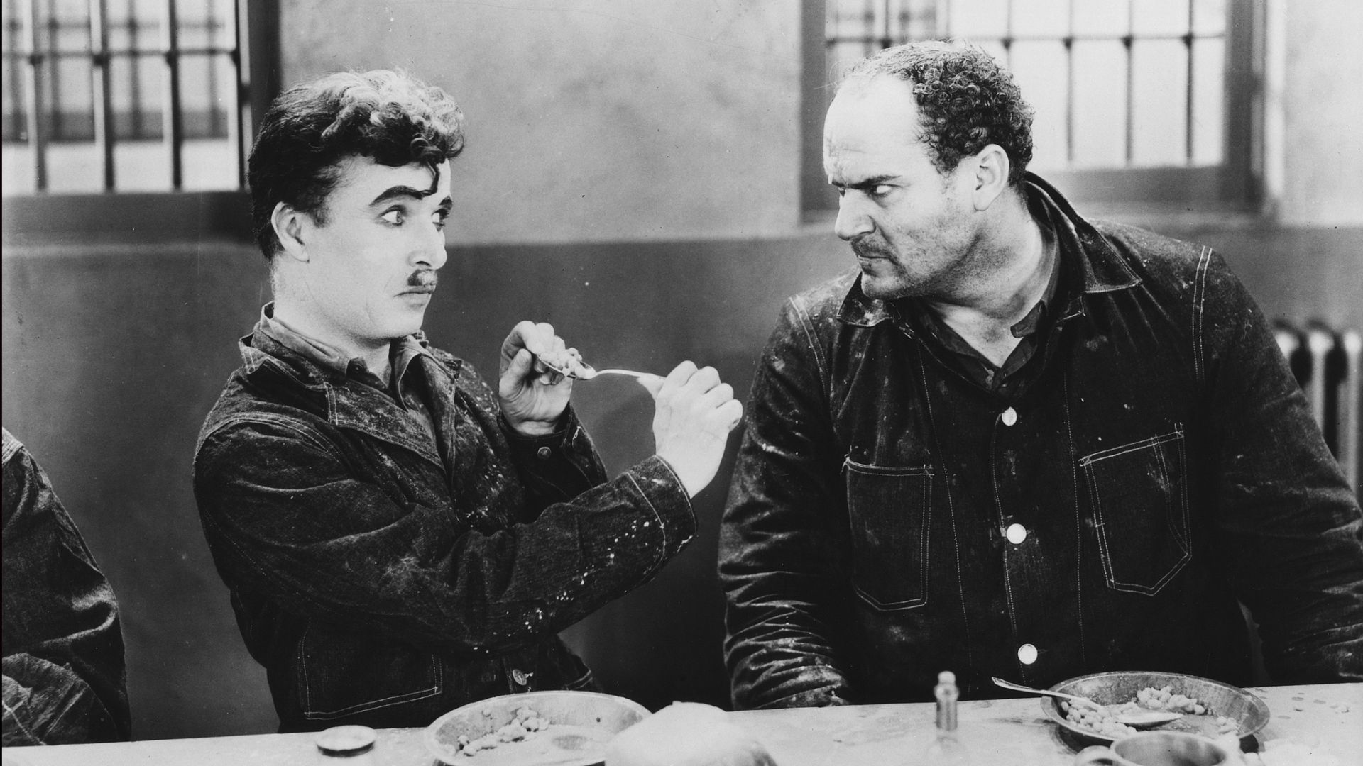 Film still of actor Charlie Chaplin in prison, flicking food at another inmate, in a scene from part-silent film 'Modern Times', 1936. /American Stock Archive/Moviepix/Getty Images
