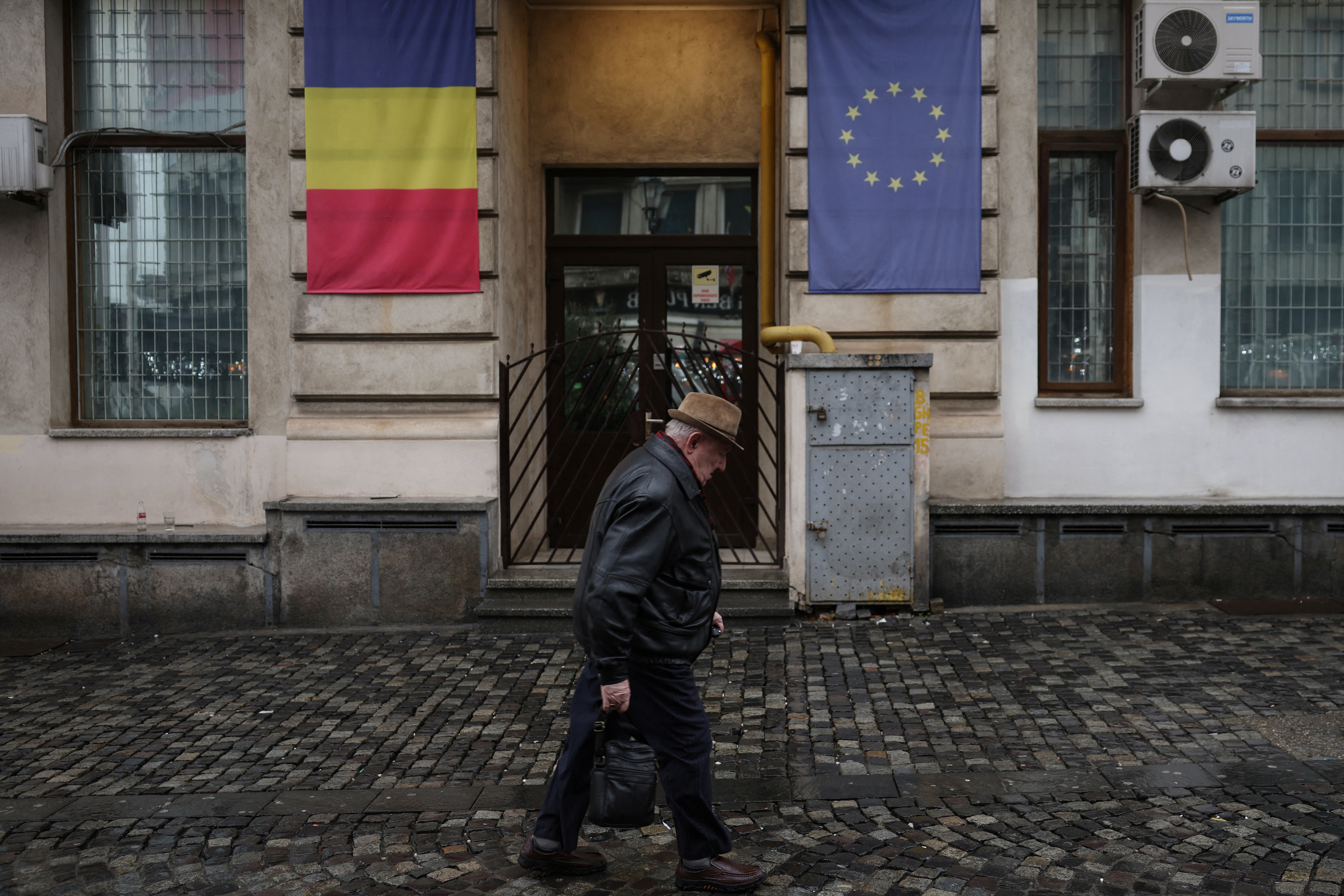 A man walks past a building with Romanian and EU flags in Bucharest. He, like other Romanians, won't be electing a president this weekend. /Louisa Gouliamaki/Reuters
