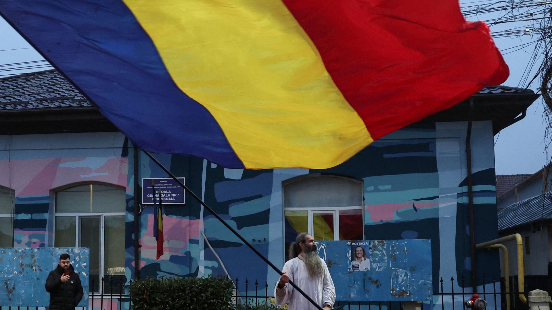 A supporter of the Romanian presidential candidate Calin Georgescu waves the country's flag outside his voting station after the annulation of the presidential elections. /Louisa Gouliamaki/Reuters
