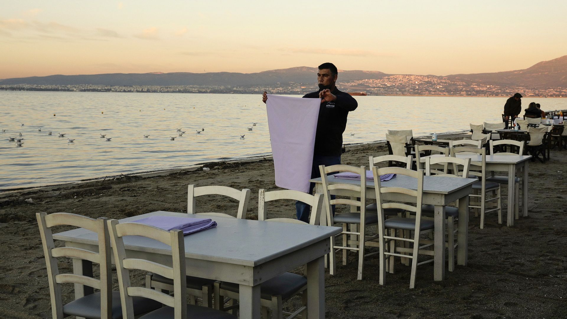 A waiter folds a tablecloth at an empty seaside restaurant in the eastern suburb of Peraia in Thessaloniki, Greece. /Konstantinos Tsakalidis/Bloomberg via Getty Images
