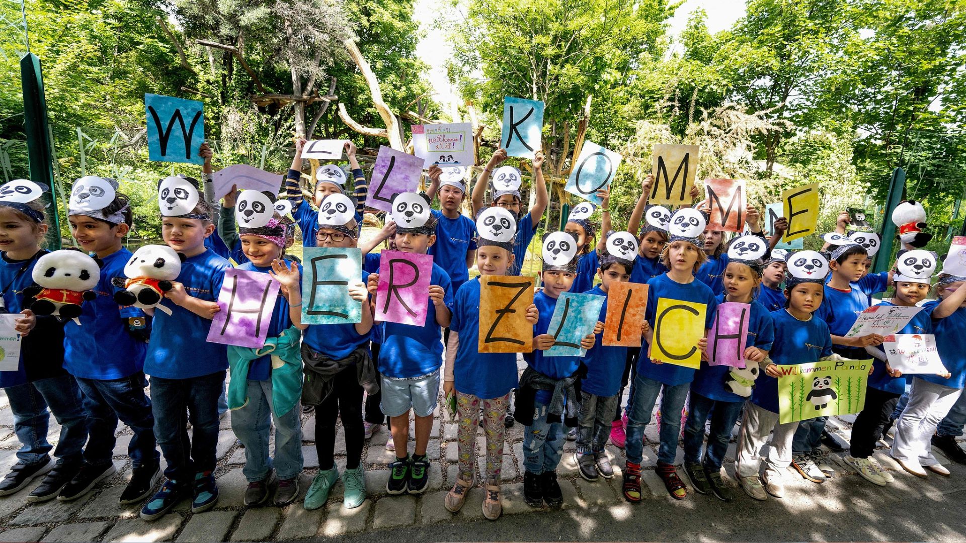 Children in anda masks hold up placards during a ceremony to welcome the pair to the Schoenbrunn Zoo in Vienna. /Joe Klamar/via CFP
