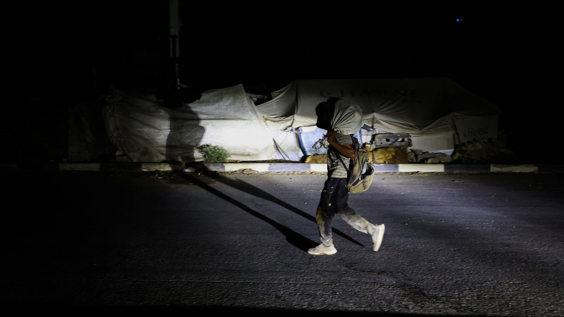 A Palestinian man walks back, carrying a parcel collected from a food aid distribution point set up by the privately-run Gaza Humanitarian Foundation on the Sala. /Eyad Baba]/AFP
