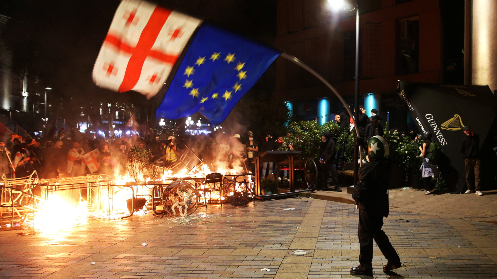A protester waves Georgian and EU flags in front of a burning barricade in Tbilisi, Georgia. /Irakli Gedenidze/Reuters