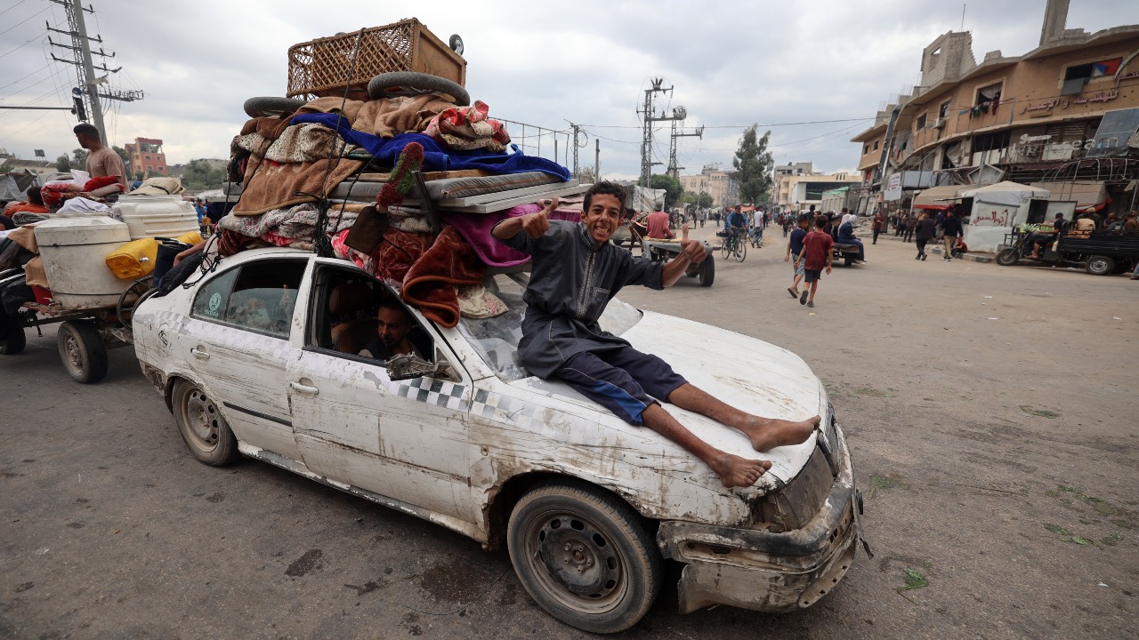 A young boy sits on a car as displaced Palestinians drive through the Nuseirat refugee camp in the central Gaza Strip, as they return to Gaza City. /Eyad Baba/AFP
