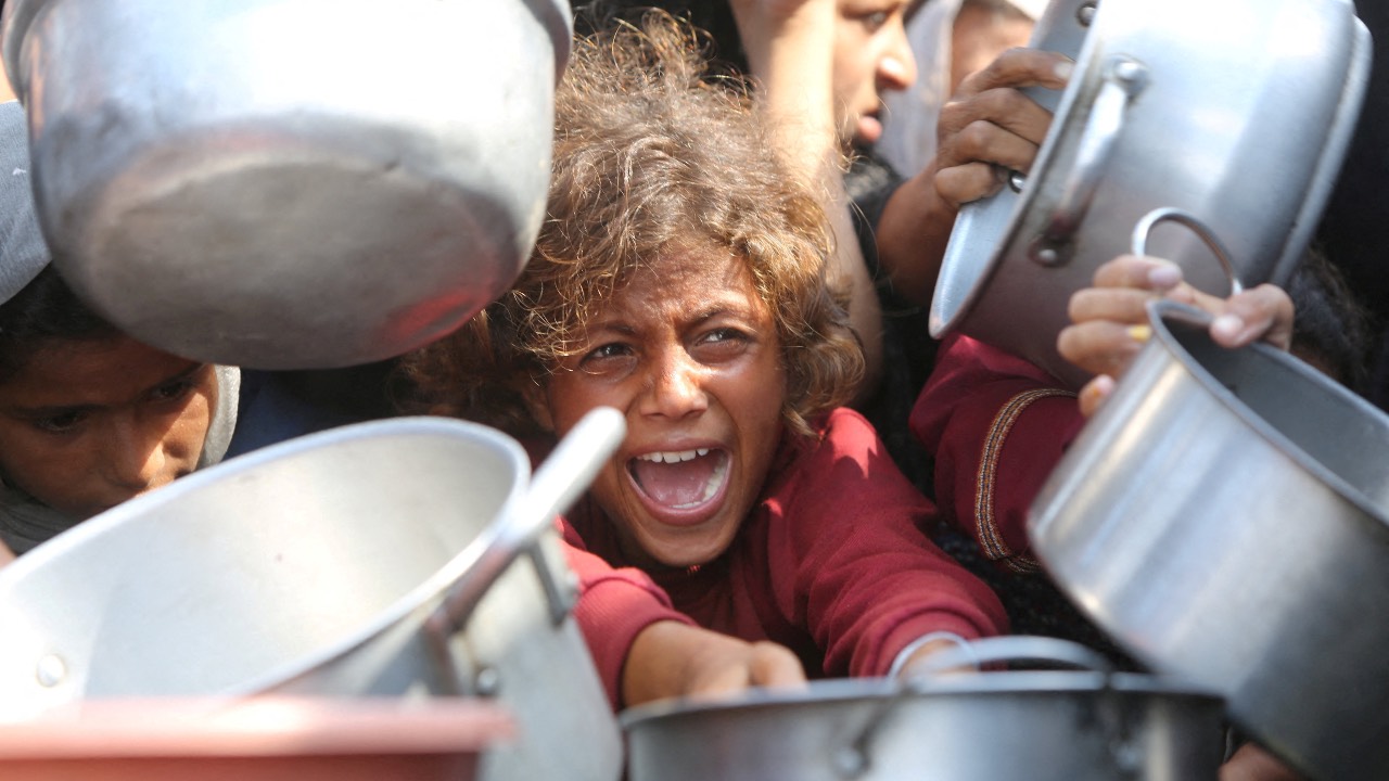 A child reacts surrounded by pots as Palestinians wait to receive food from a charity kitchen in Khan Younis, southern Gaza Strip. /Hatem Khaled/Reuters