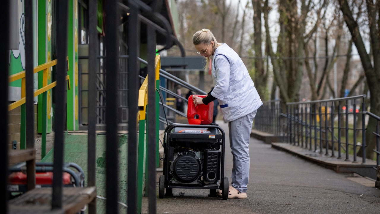 A woman fills petrol into a power generator to produce electricity for a pharmacy after critical civil infrastructure was hit by a recent Russian missile and drone attack. /Thomas Peter/Reuters