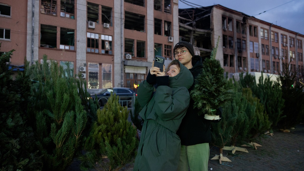 A couple poses with a fir tree also known as a Christmas tree at a street market near damaged buildings in Kyiv on Christmas Eve. 
Tetiana Dzhafarova/AFP