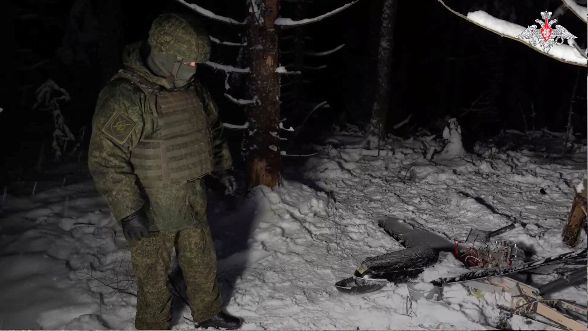 A Russian service member stands next to the remains of a drone, which, according to the Russian Defence Ministry, was downed during the repelling of an alleged Ukrainian attack on the Russian presidential residence in the Novgorod Region, in an unknown location in Russia. /Russian Defence Ministry/Handout 
