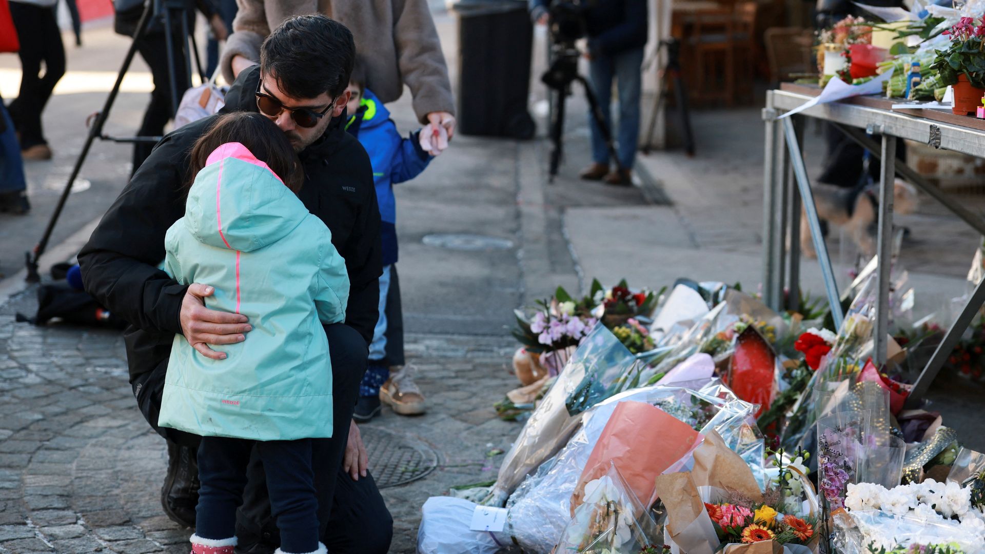 A man embraces a child next to the tributes laid for the victims outside the bar, on Friday. /Stephanie Lecocq/Reuters
