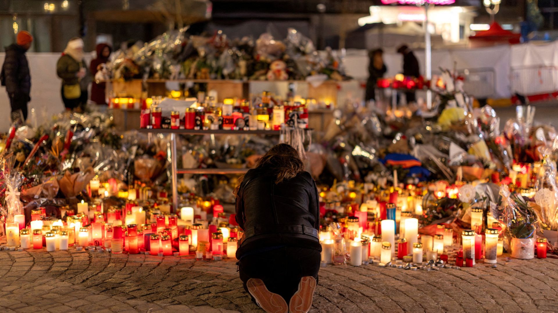 A woman lights a candle at a makeshift memorial outside the 'Le Constellation