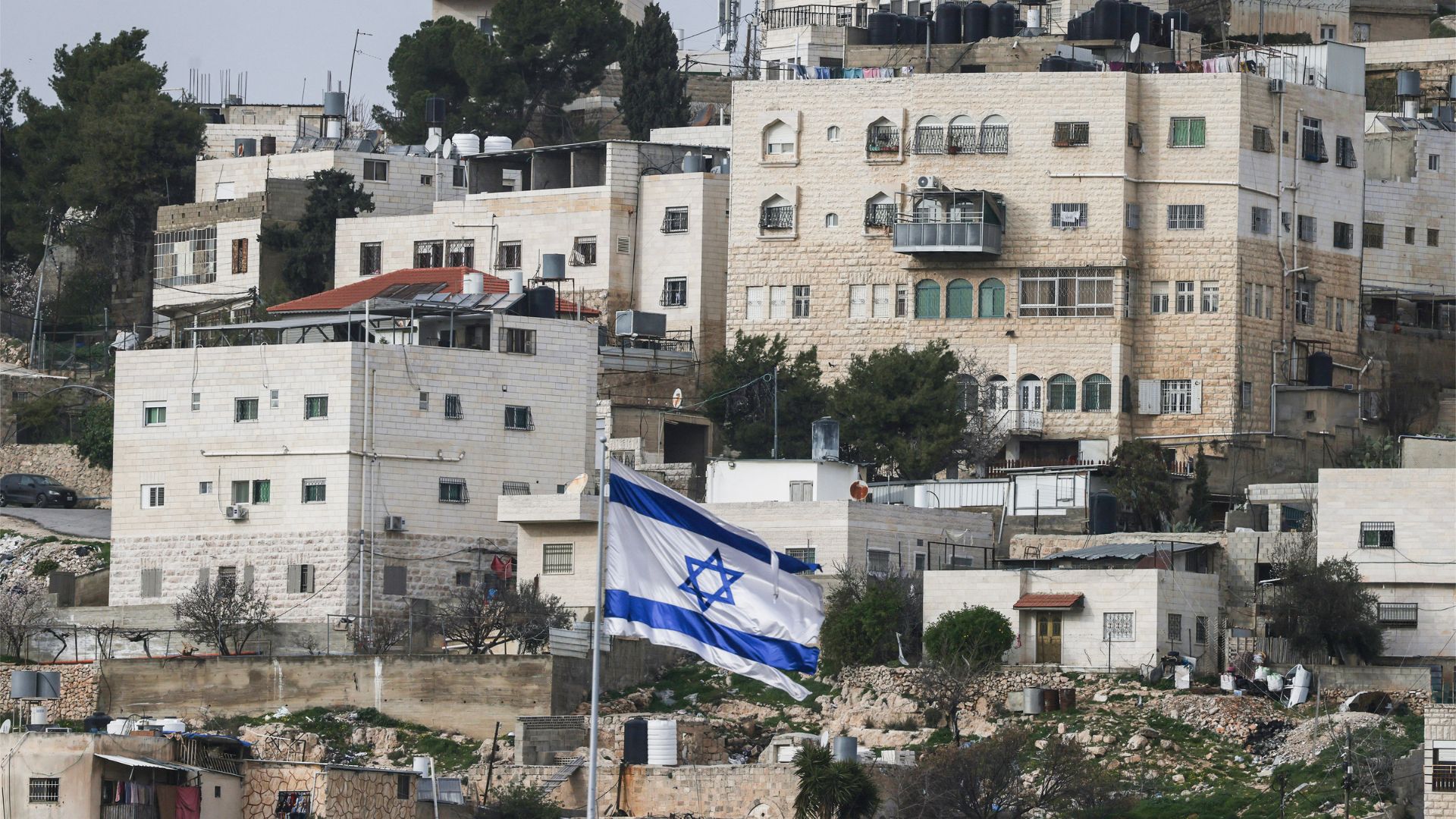 An Israeli flag fluttering above the Israeli settlement of Beit Romano (unseen), with Palestinian buildings in the background, in the Israeli-occupied West Bank city of Hebron on February 9. /Hazem Bader/AFP