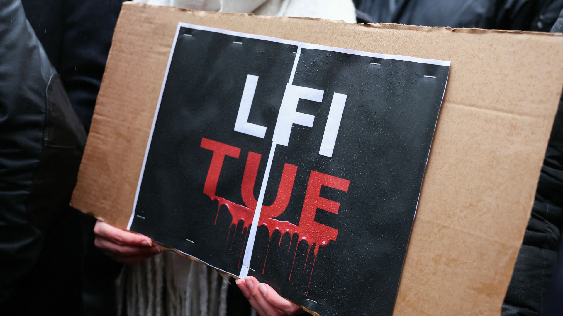 A demonstrator holds a placard reading 'LFI kills' at a Paris rally after the death of Deranque.
/Alain Jocard/AFP
