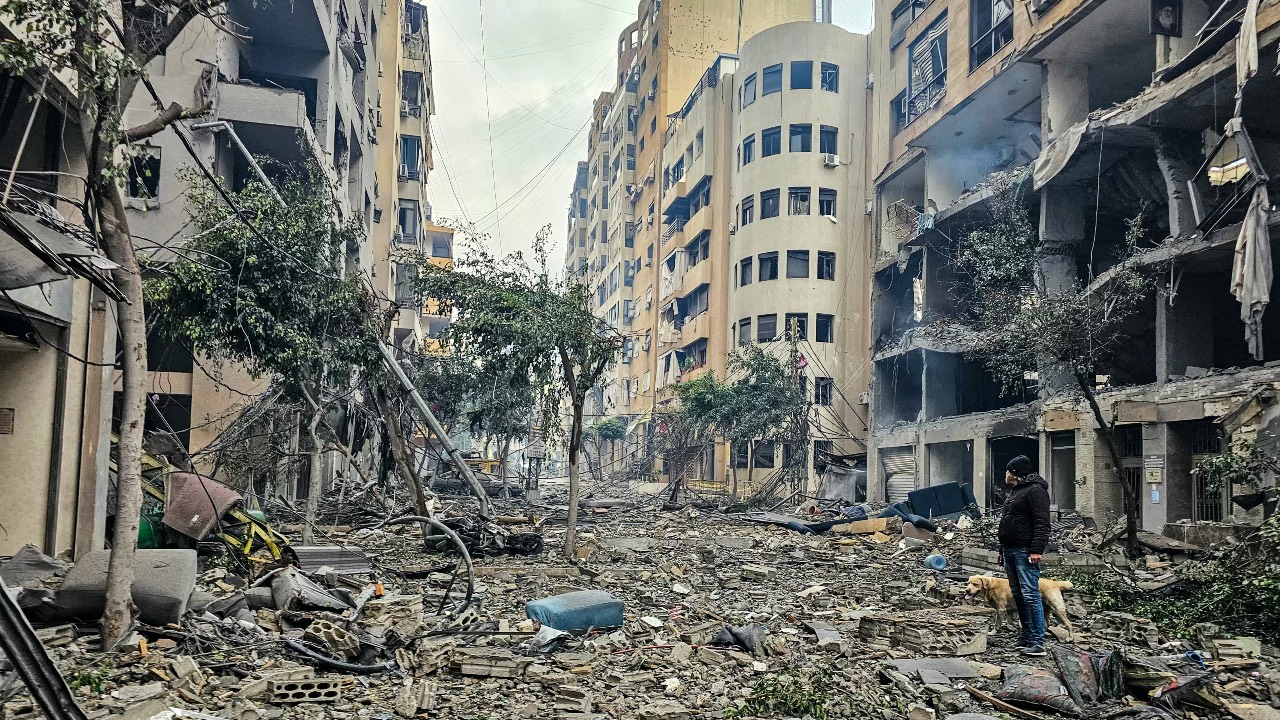 A man and his dog walk across the rubble of a building at the site of an Israeli airstrike in Beirut's southern suburb Haret Hreik. /AFP