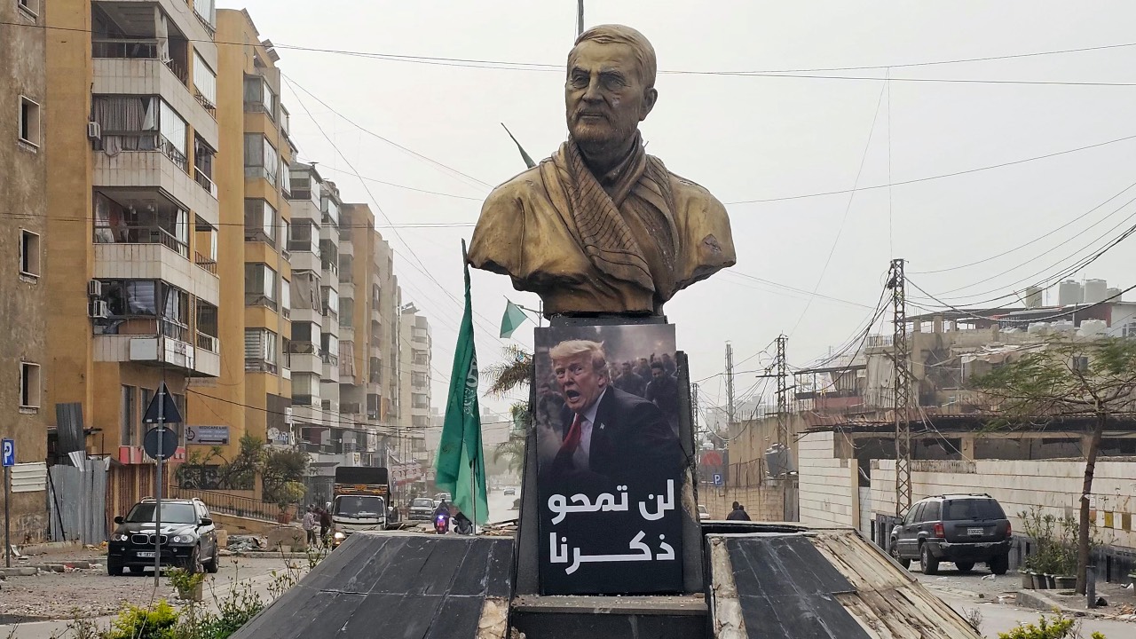 A sign depicting US President Donald Trump, with the caption 'you will not erase our memory' in Arabic, is displayed before a memorial depicting Qassem Soleimani, the slain commander of the Quds Force of Iran's Islamic Revolutionary Guards Corps who was killed by a US airstrike in 2020, along the road leading to Beirut International Airport in Beirut. /AFP