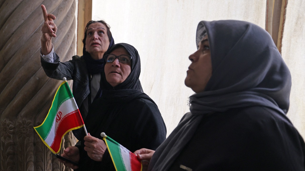 Visitors, while holding Iran's national flags, inspect the damaged interiors of the historic Golestan Palace in the Iranian capital Tehran. /Atta Kenare/AFP