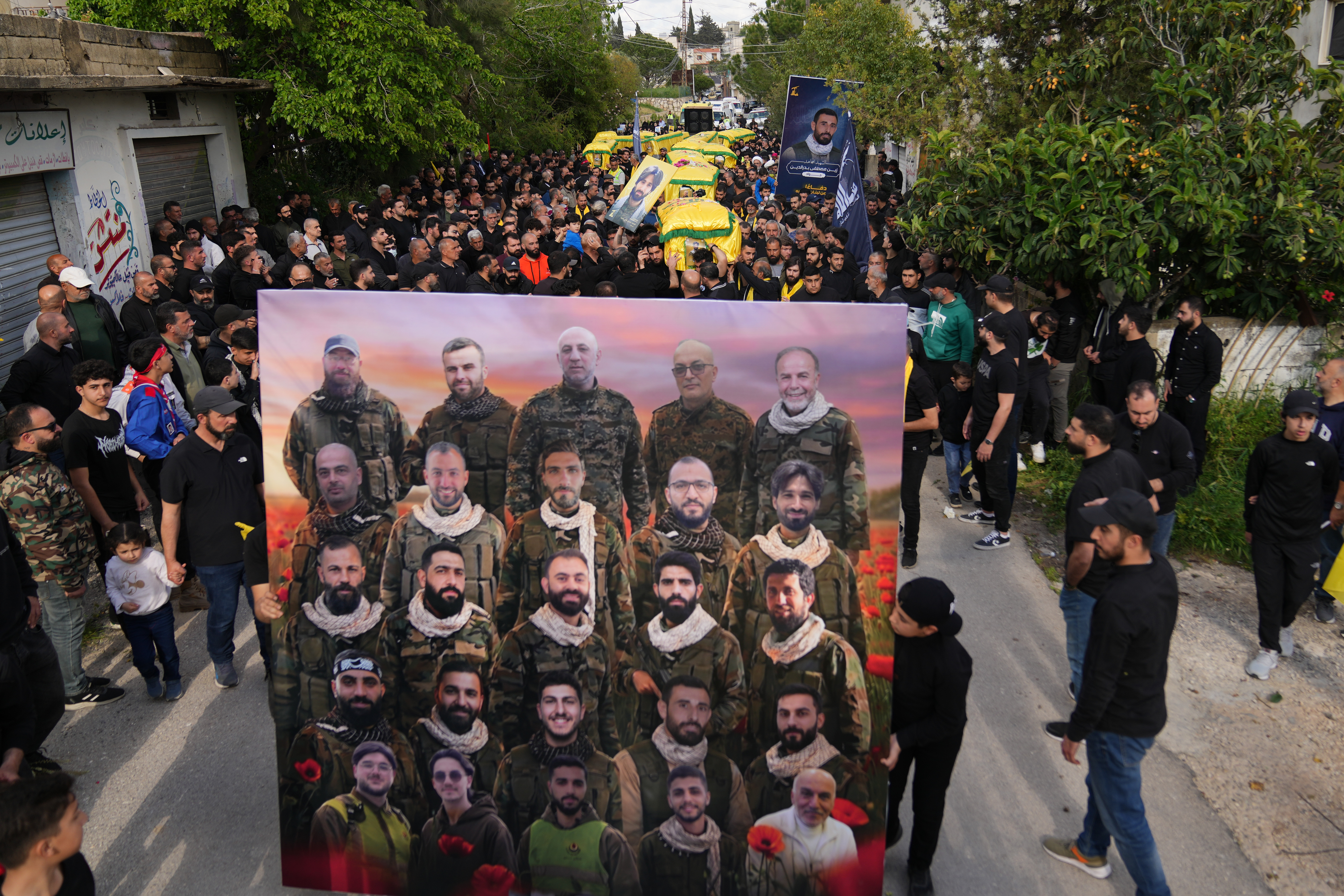 Mourners carry a poster showing Hezbollah fighters and paramedics, who were killed before the ceasefire in the war between Hezbollah and Israel, during a mass funeral procession in the southern village of Kfar Sir, Lebanon on April 21. /Hassan Ammar/AP