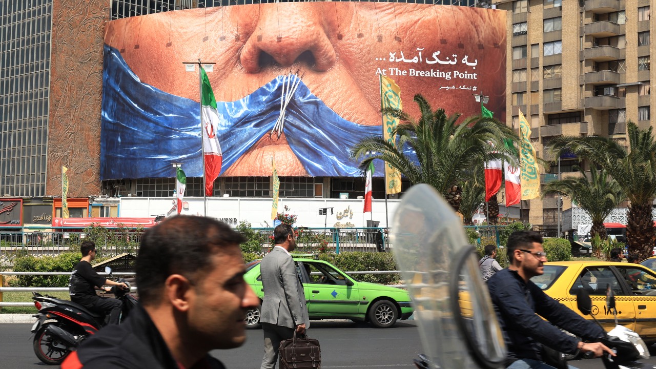 Commuters make their way past an anti-US billboard referring to President Donald Trump and the Strait of Hormuz, installed on a building at the Valiasr Square in Tehran. /AFP