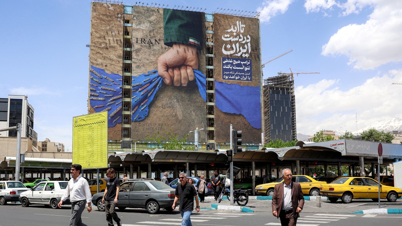 People cross a street near a billboard on the facade of a building depicting the Strait of Hormuz with a caption in Persian reading 'Forever in Iran’s hand,' at Vanak Square in Tehran. /AFP