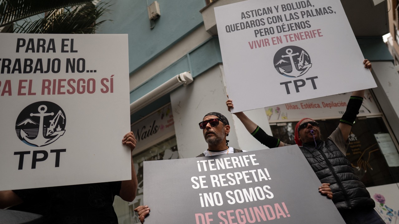 Dockers hold banners reading 'Workers of Tenerife port - TPT (Trabajadores del Puerto de Tenerife) - Respect Tenerife - we are not second-class' as they protest against the arrival of a cruise ship affected by hantavirus in Santa Cruz de Tenerife. /Jorge Guerrero/AFP
