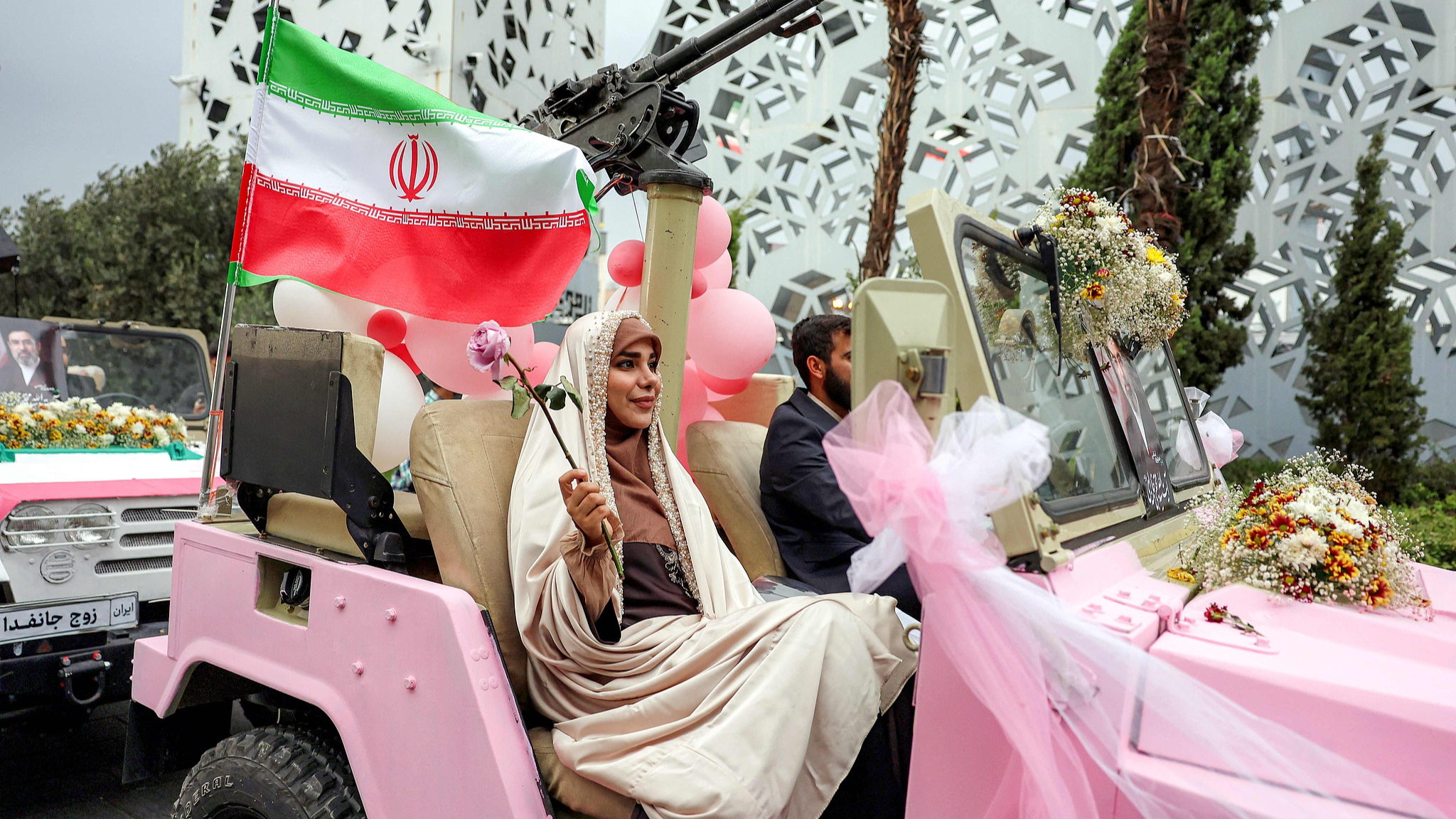A bride and groom couple rides in a military jeep arriving for a public mass wedding ceremony at Imam Hossein Square in Tehran on May 18, 2026. /AFP