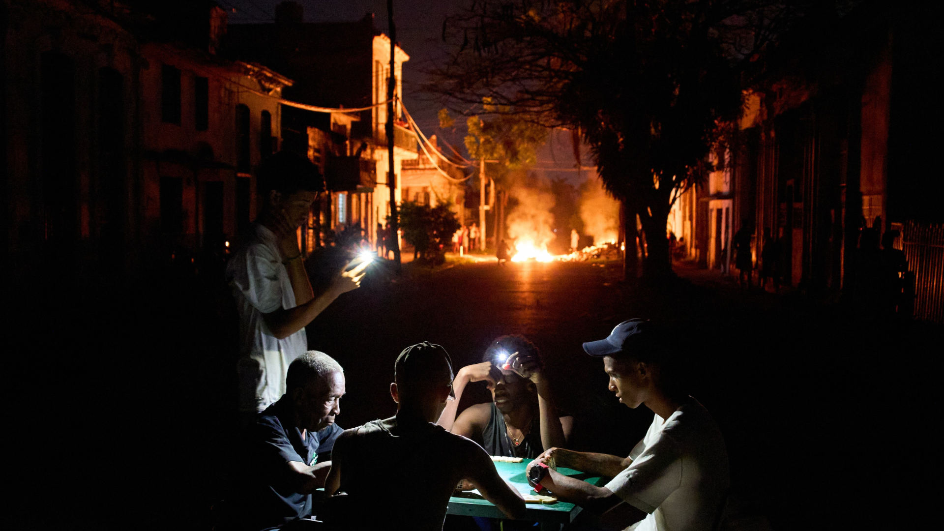 Dominoes players illuminate their game with mobile phones as a fire set up by residents protesting against prolonged power outages burns on a street in Havana, Cuba. /Ramon Espinosa/ AP Photo