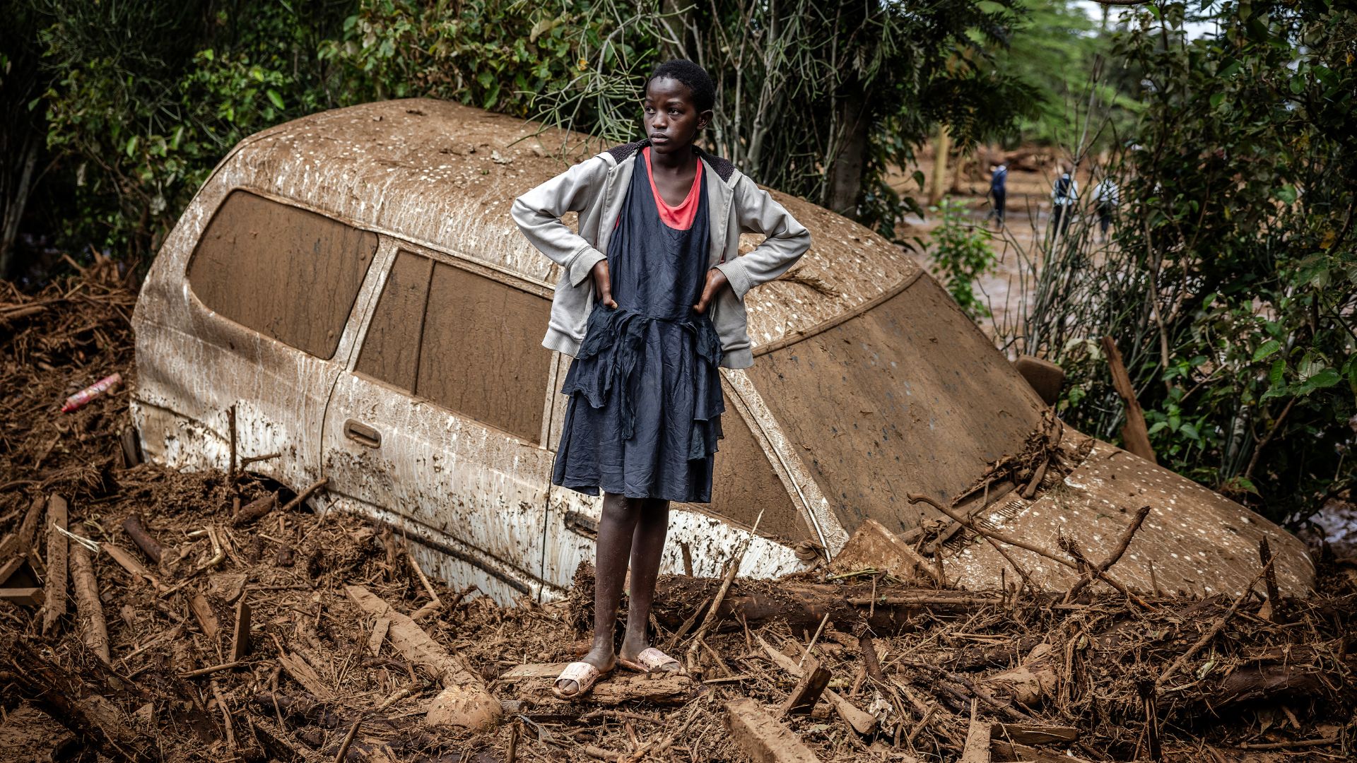 A girl stands next to a damaged car buried in mud in an area heavily affected by torrential rains and flash floods, compounded by El Nino, in the village of Kamuchiri, Kenya. /Luis Tato/AFP
