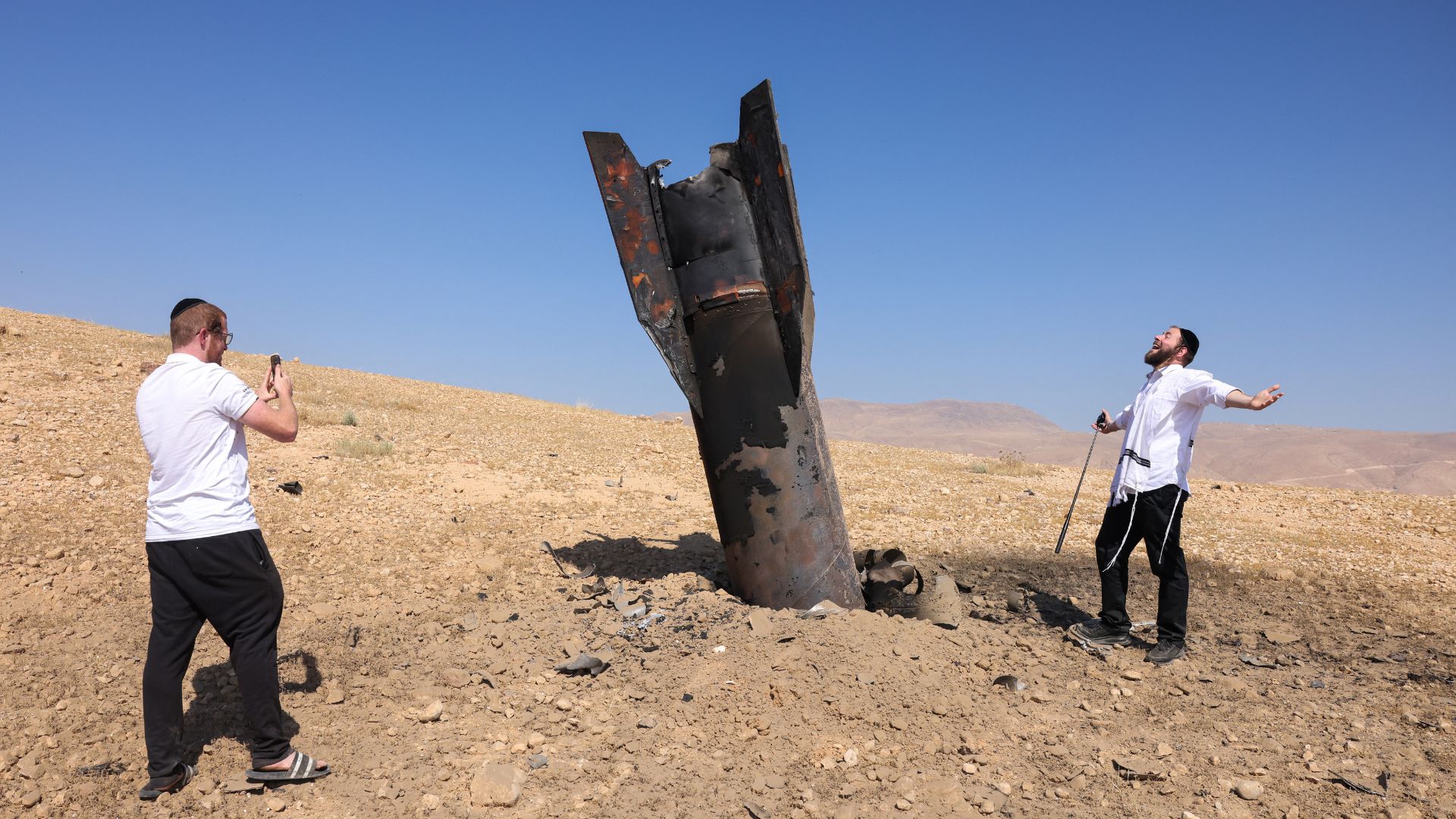 A man poses for a photo next to a fallen rocket half-buried in the ground on the outskirts of Jericho on June 8, following Iranian and Iran-backed Houthi rebel attacks. /Ahmad Gharabli/AFP
