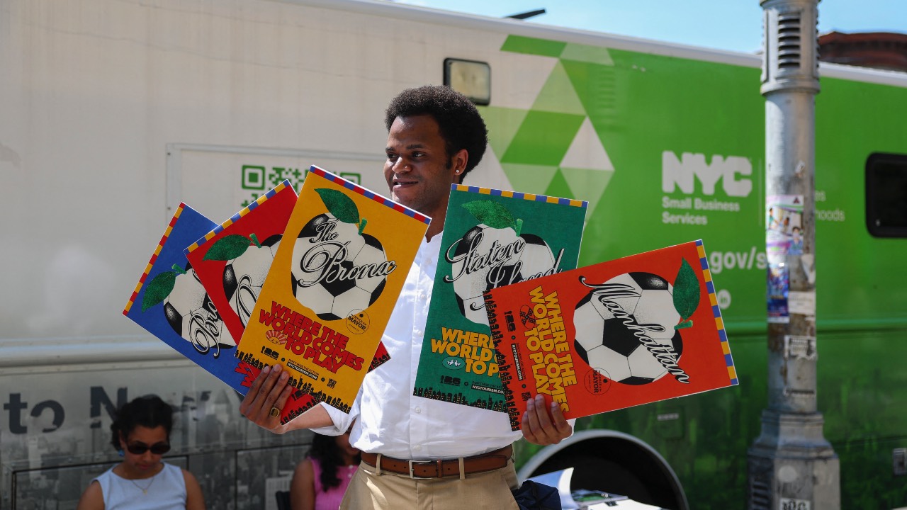 Jacques Brunvil of the NYC Department of Small Business Services holds up 2026 FIFA World Cup poster during an outreach event hosted by the NYC Department of Small Business Services in New York’s 'Little Haiti' neighborhood. /Angela Weiss/AFP