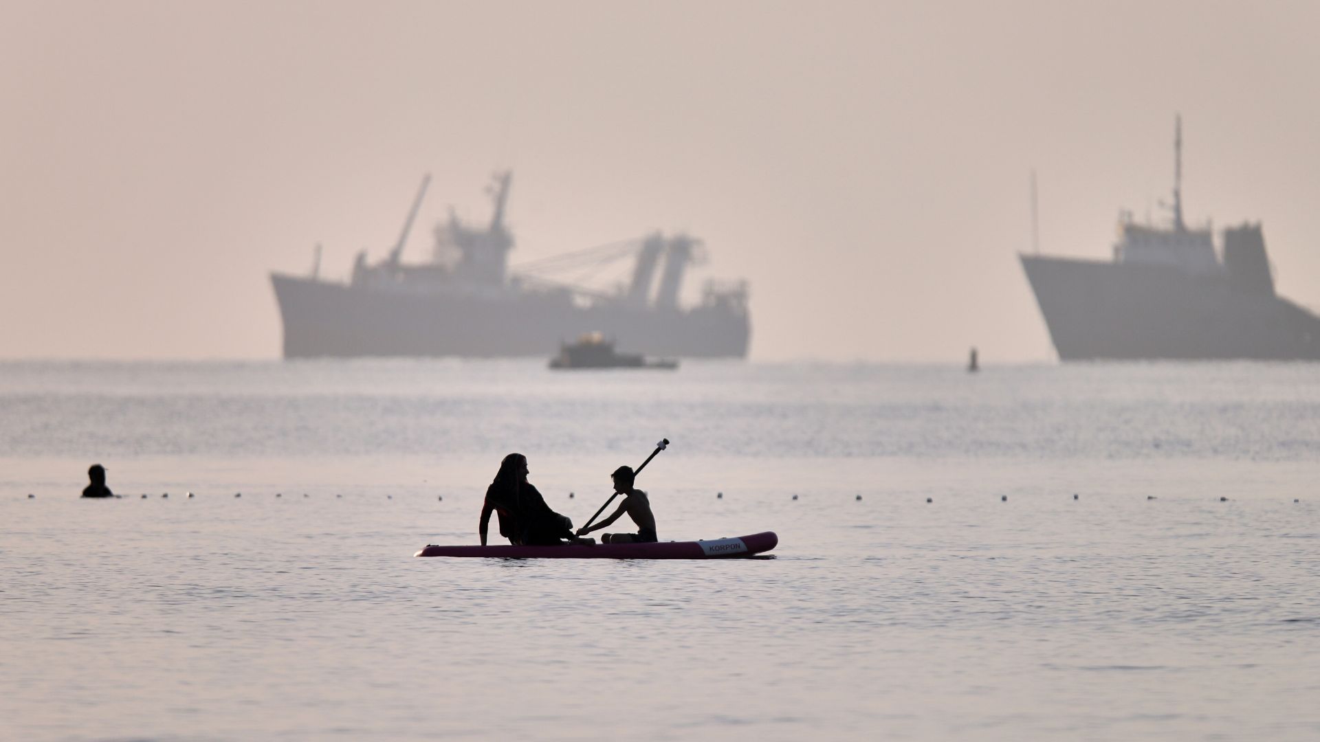 People ride a paddleboard as cargo and service vessels are anchored in the Strait of Hormuz off Bandar Abbas, Iran, on June 1. /Amirhosein Khorgooi/ISNA via AP