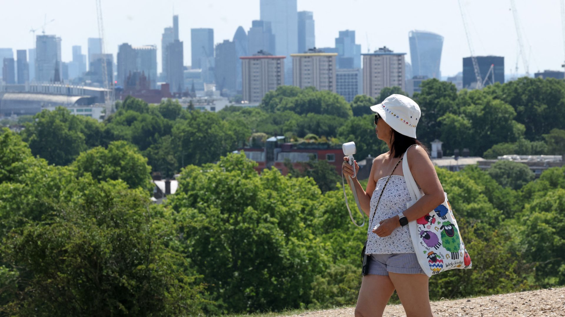 A woman uses a hand-held fan to cool down on London's Primrose Hill. /AFP. 