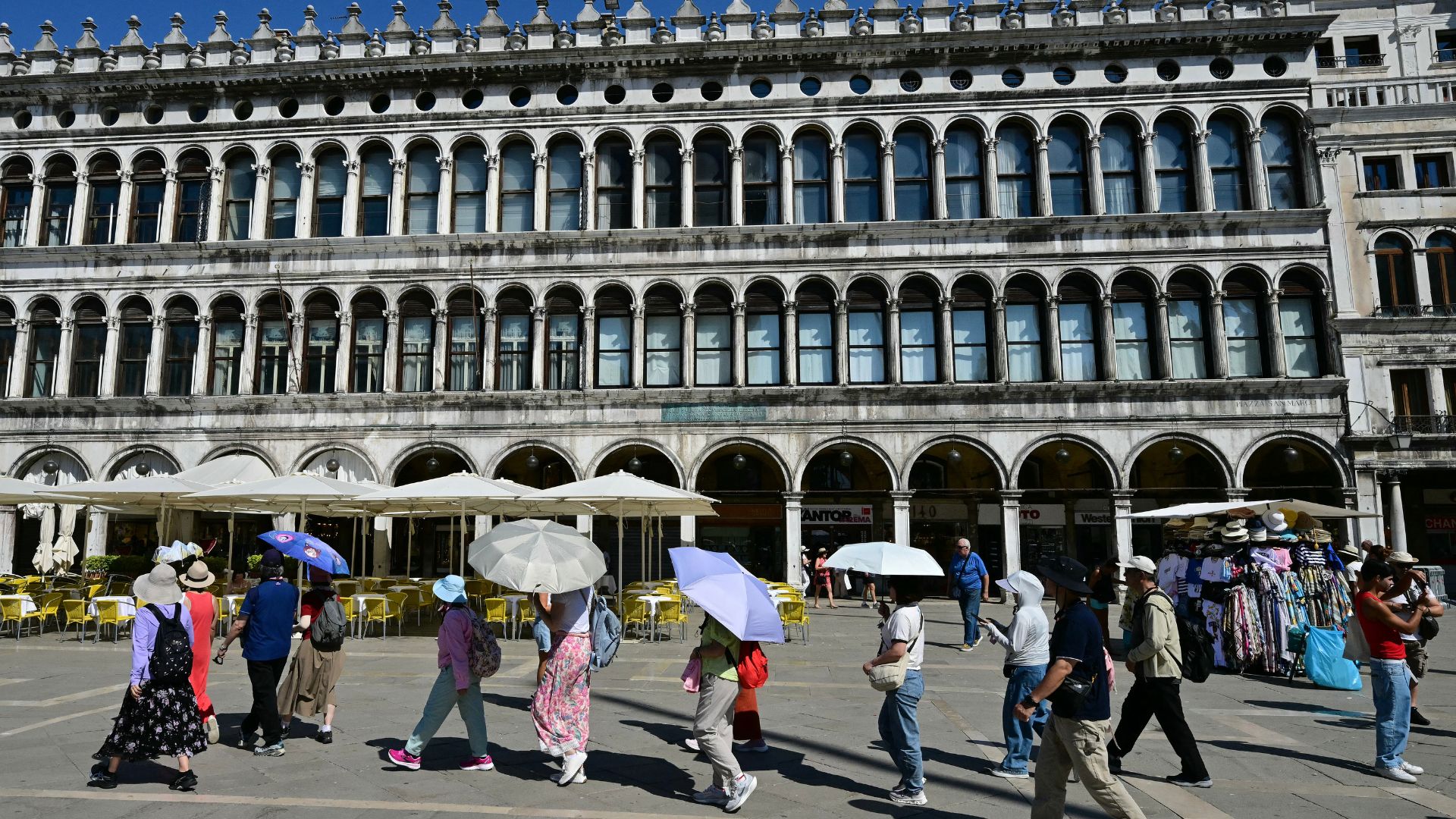 Tourists use umbrellas to shield themselves from the sun in Saint Mark square, Venice. /AFP.