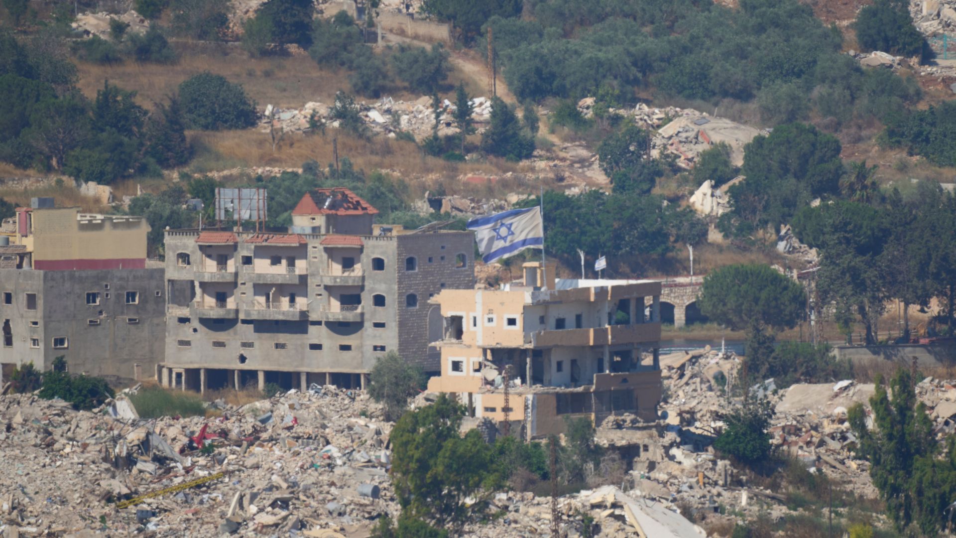 An Israeli flag tops a destroyed building in southern Lebanon, as seen from northern Israel, following strikes in the area. AP Photo/Ohad Zwigenberg. 