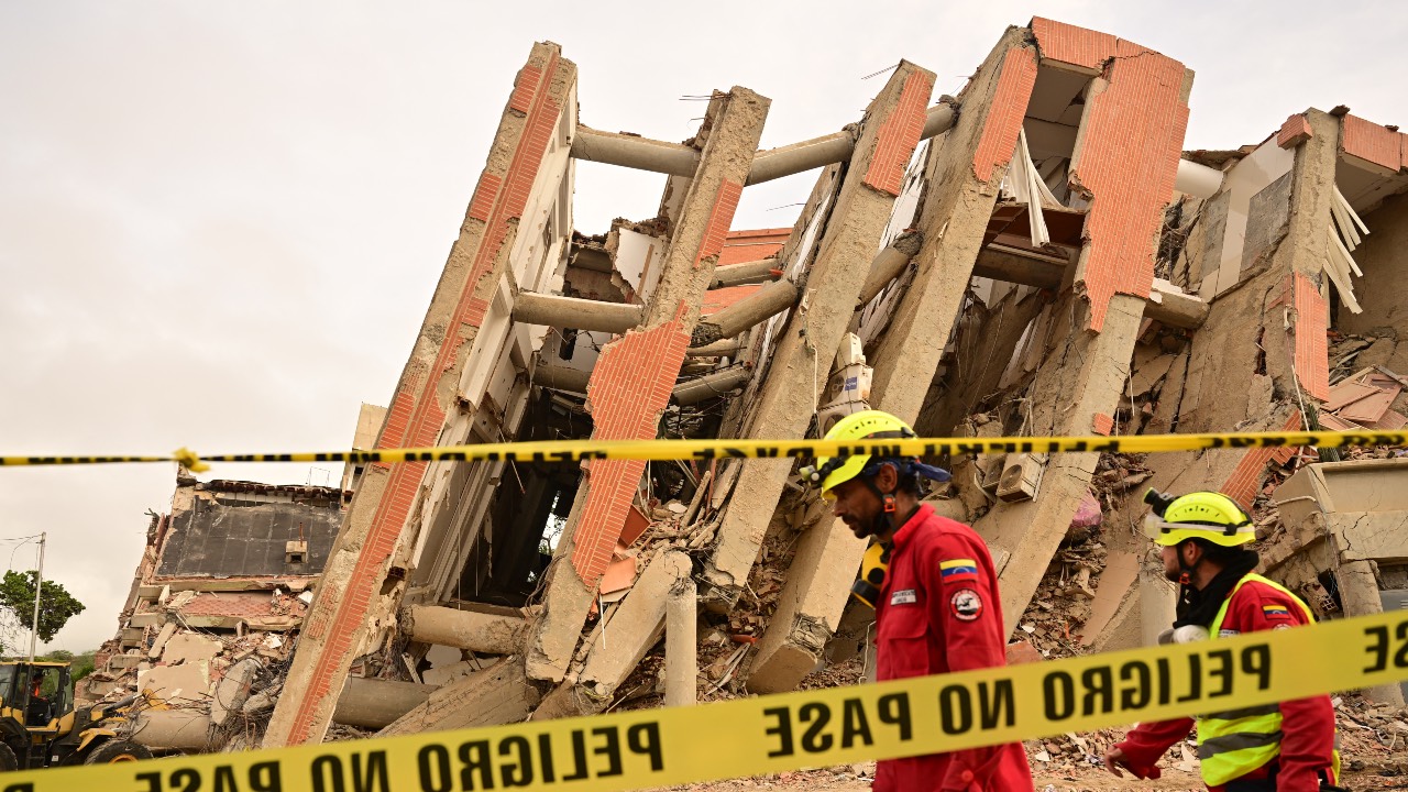 Rescue workers walk past a collapsed building cordoned off with tape reading 'Do not cross' in Catia La Mar, La Guaira state, on the outskirts of Caracas. /Martin Bernetti/AFP
