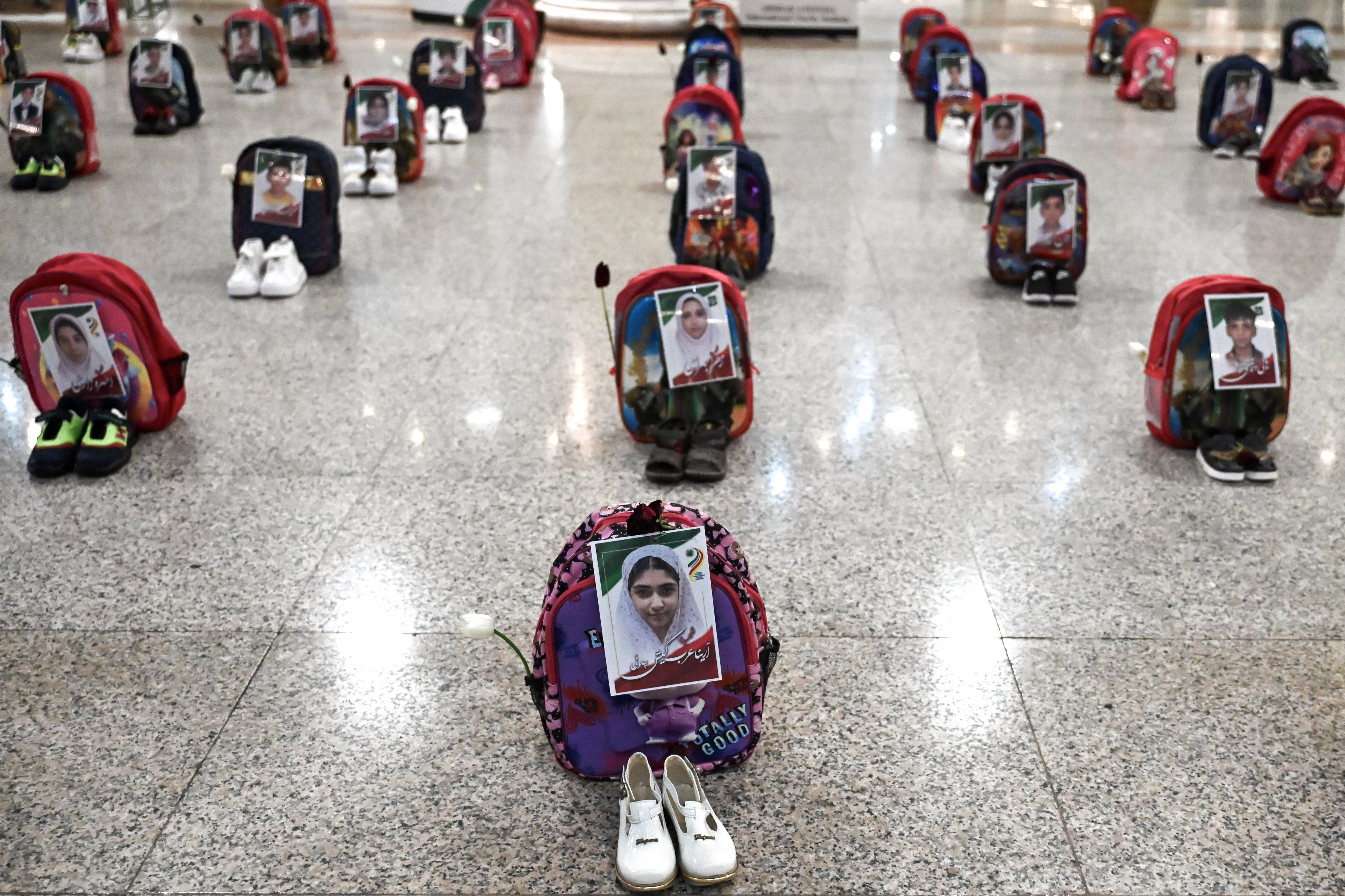 Portraits of schoolchildren killed in an air strike in Minab in February 2026 are pasted onto backpacks displayed alongside shoes at Hashemi Nejad International Airport in Mashhad on July 8, 2026. /AFP