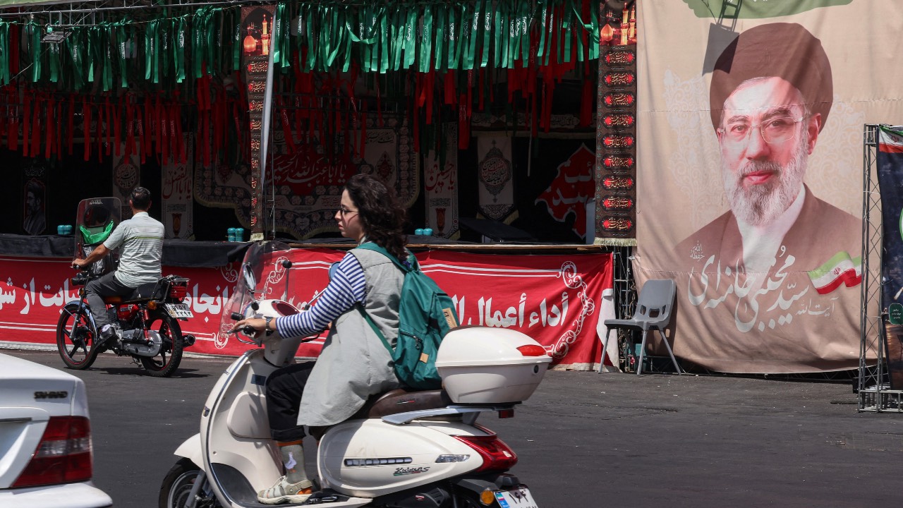 A woman rides a motorcycle past a banner of Iran's Supreme Leader Mojtaba Khamenei at Valiasr Square in Tehran. /Atta Kenare/AFP