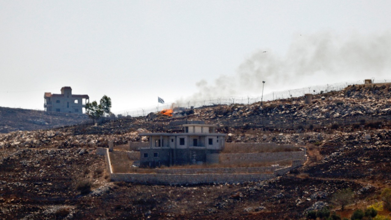 An Israeli flag is seen over the burnt fields of the border village of Mais al-Jabal, burnt during Israeli military operations. /Ammar Ammar/AFP