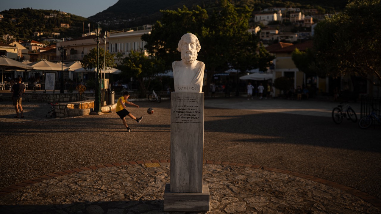 A child plays football next to a marble bust of ancient Greek poet Homer in the central square of Vathy, on the island of Ithaca, in the Ionian Sea. /Angelos Tzortzinis/AFP