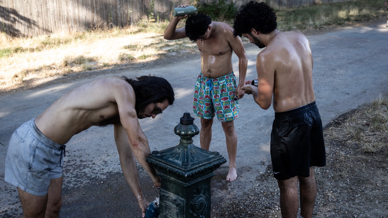 People fill their water bottles and cool off by a water fountain during a heatwave at the Bois de Vincennes park in Paris. /Behrouz Mehri/AFP
