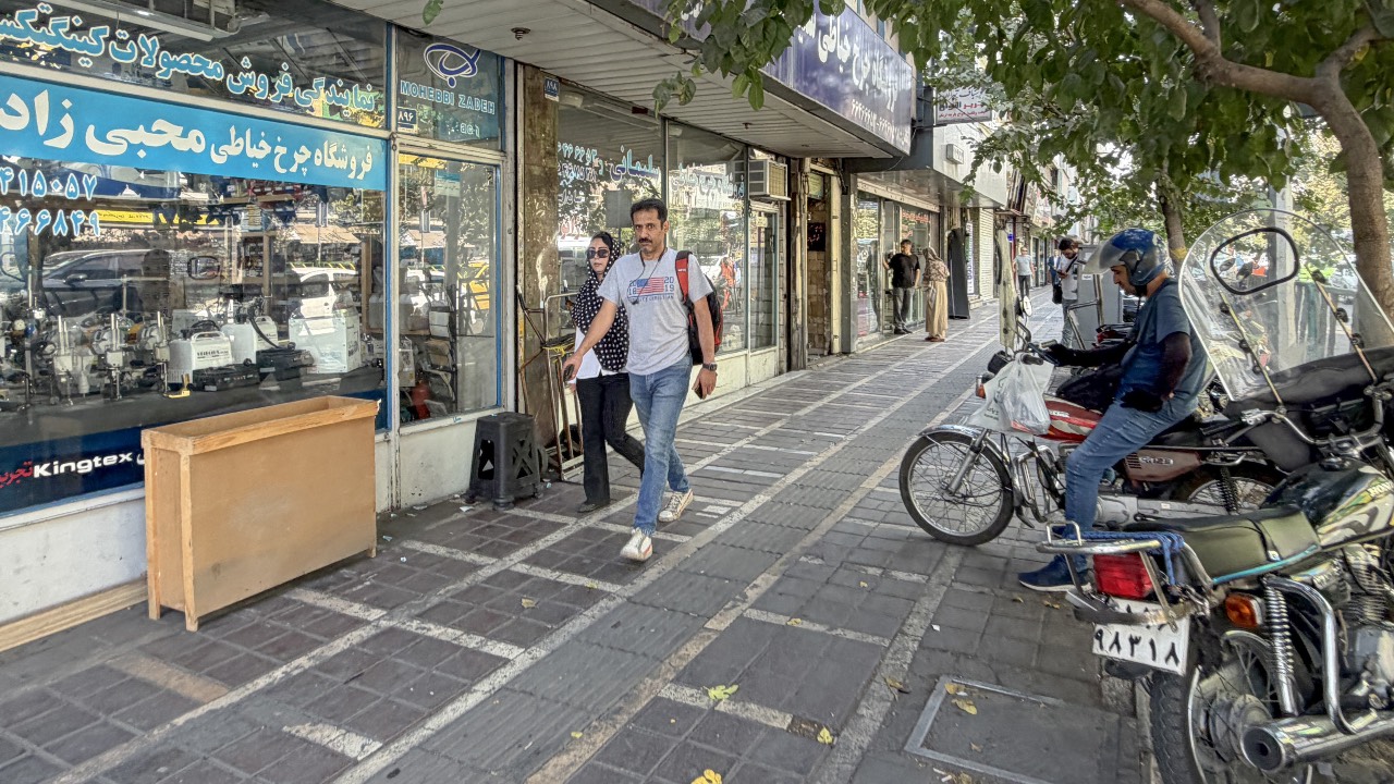 Iranians walk past shops in Tehran. /atta Kenare/AFP
