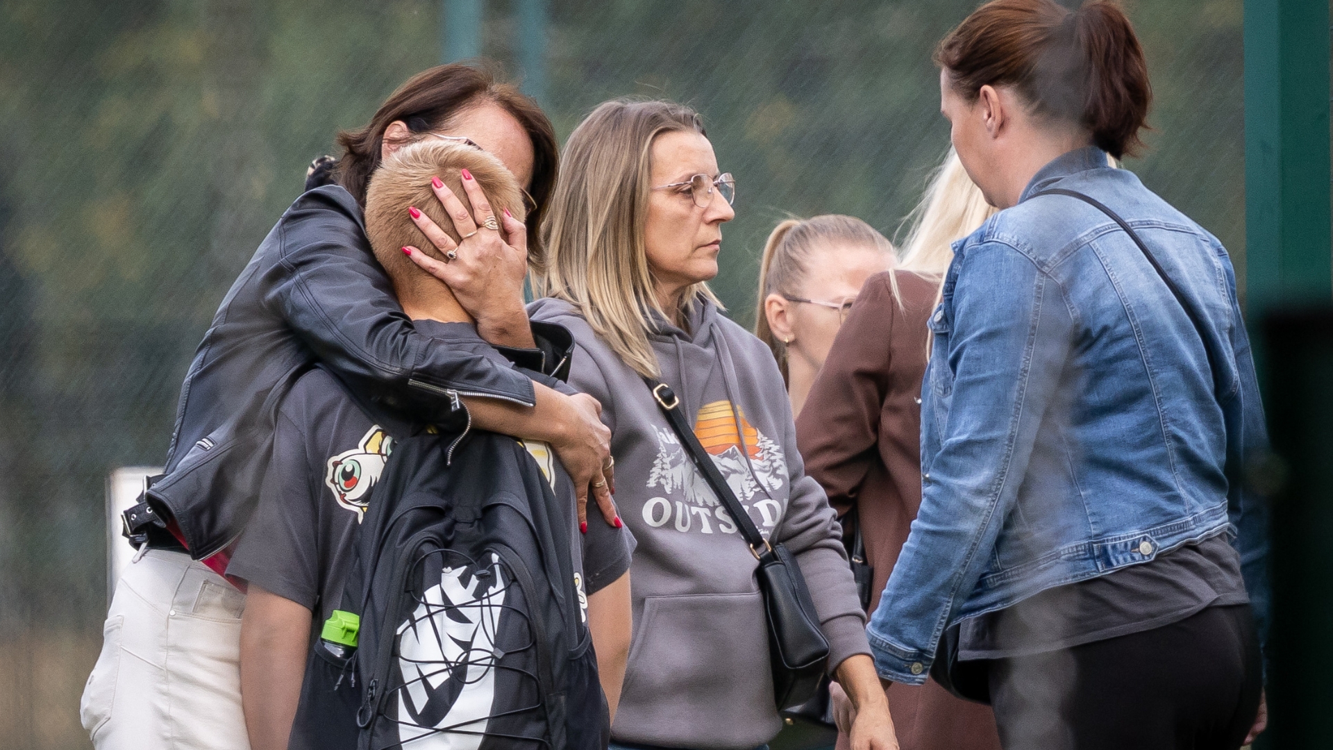 Parents hug their children outside the school where a 15-year-old fatally stabbed the caretaker and wounded two other adults on Thursday. /Wojtek Radwanski/AFP