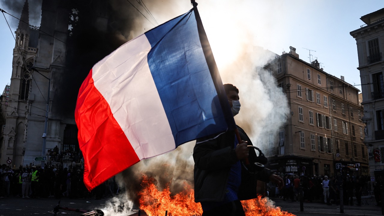A protester waving a French national flag walks past a fire during clashes prior to the start of a demonstration to protest against the 'high cost of living,' in Marseille, southern France. /Thibaud Moritz/AFP
